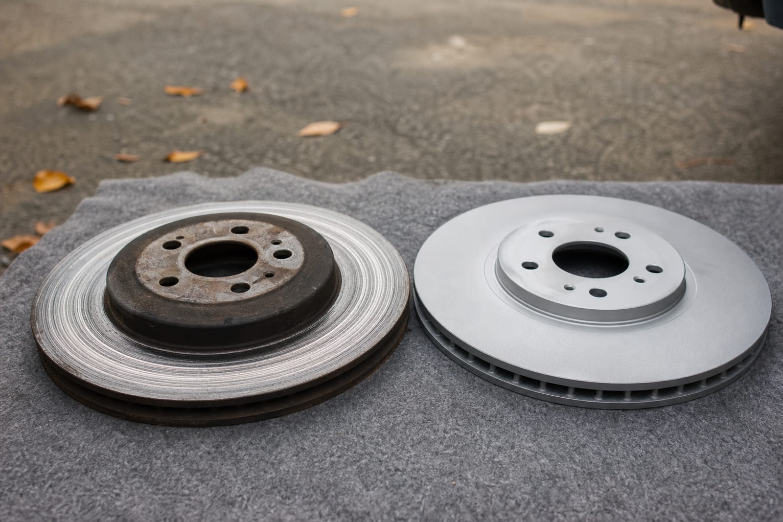 A badly scored worn brake rotor lying beside its new replacement